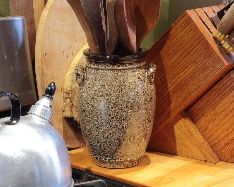 Utensil crock in Yellow Oilspot glaze with wooden cooking utensils. 